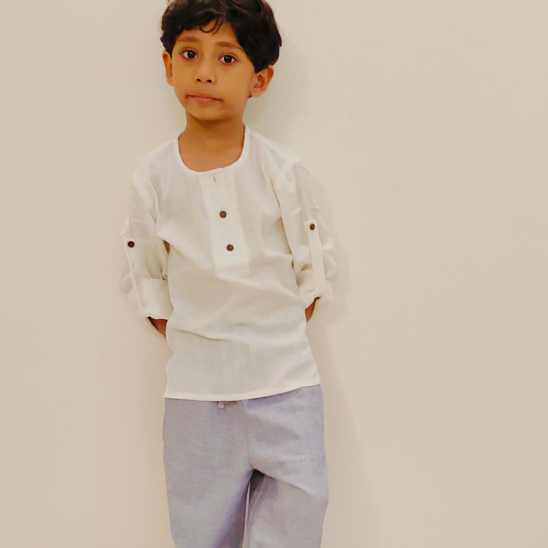 Child wearing a white shirt in cotton with buttons and light purple lounge pants against a plain background