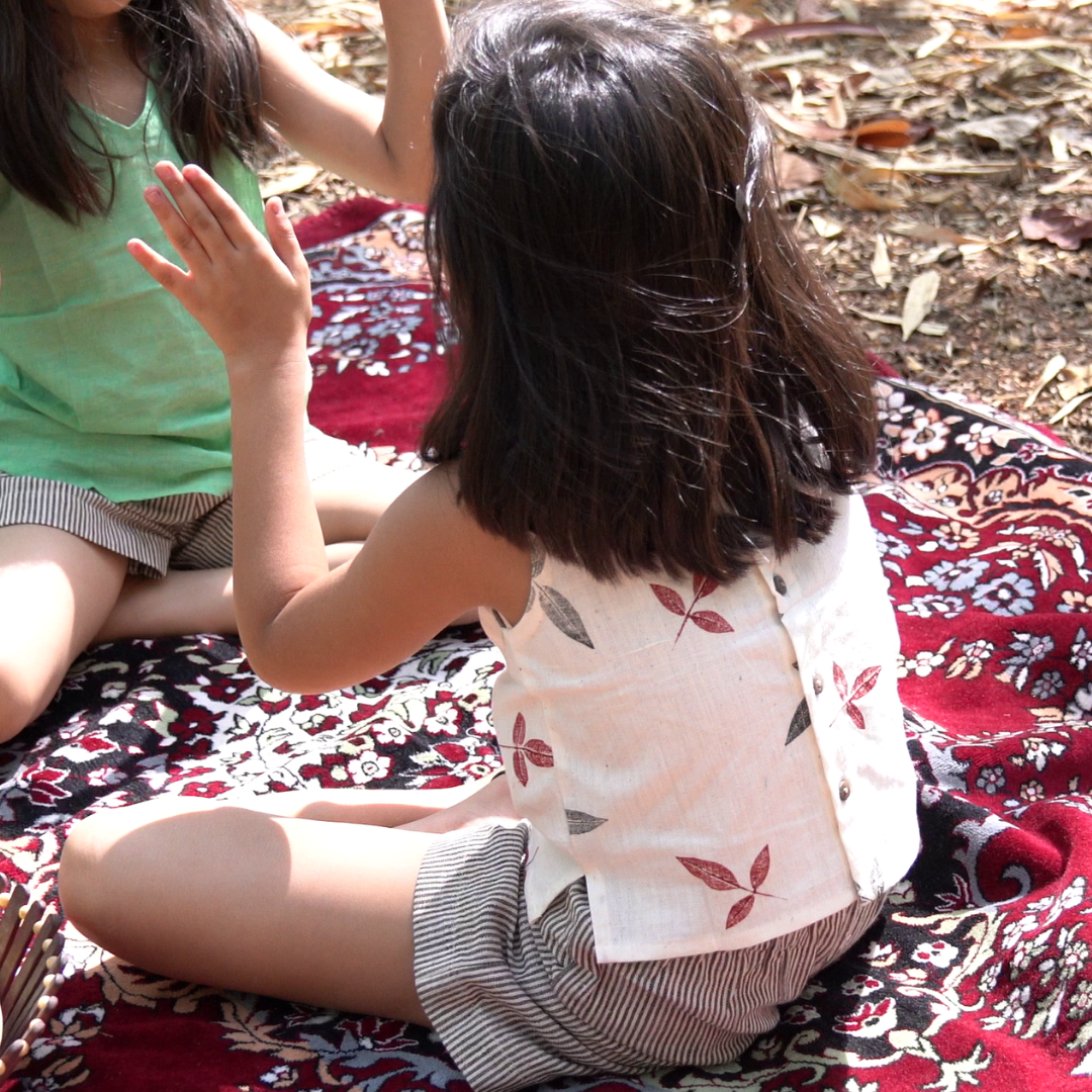 Two children wearing pure khadi clothes sitting on a patterned blanket outdoors