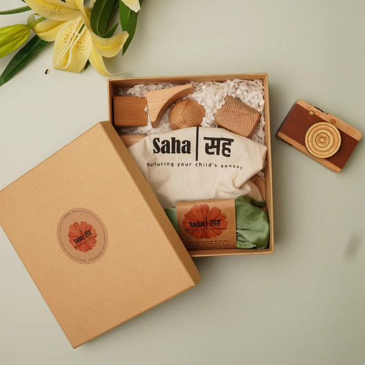 Gift box with wooden Montessori toys, organic baby clothes, and wooden camera on pale background