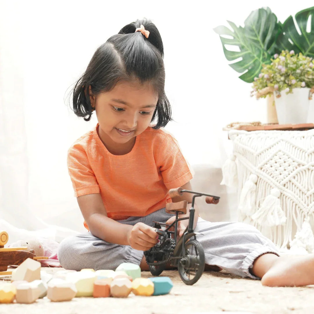 Smiling child in orange shirt playing with wooden educational toys and a bicycle model indoors