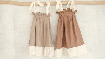Two cotton sleeveless kids dresses in natural beige and brown, hanging on a wooden rod