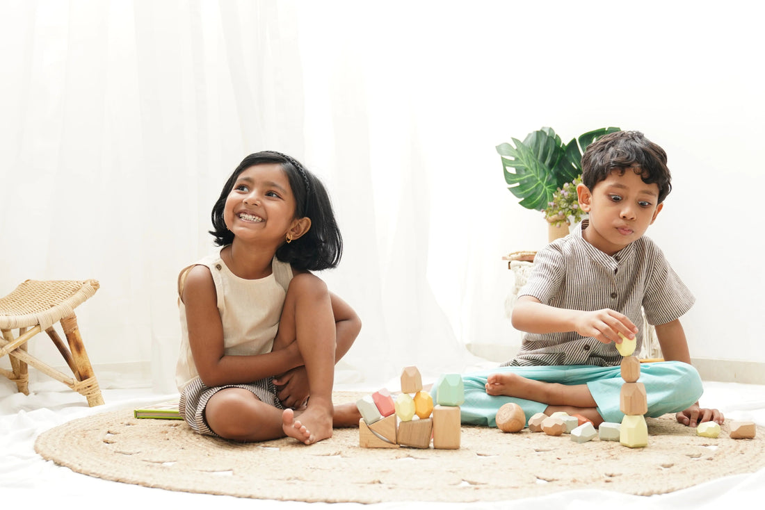 Two kids in organic cotton clothes playing with wooden educational toys on a woven rug