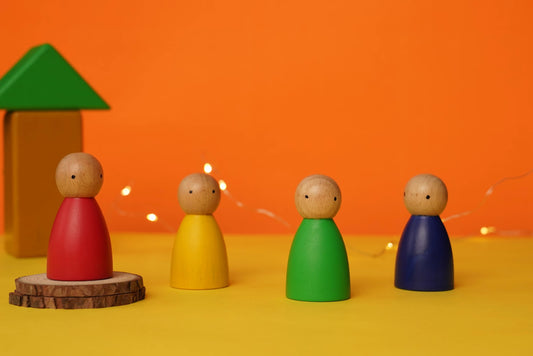 Colorful wooden peg dolls and building blocks on yellow surface with orange background, Waldorf toys