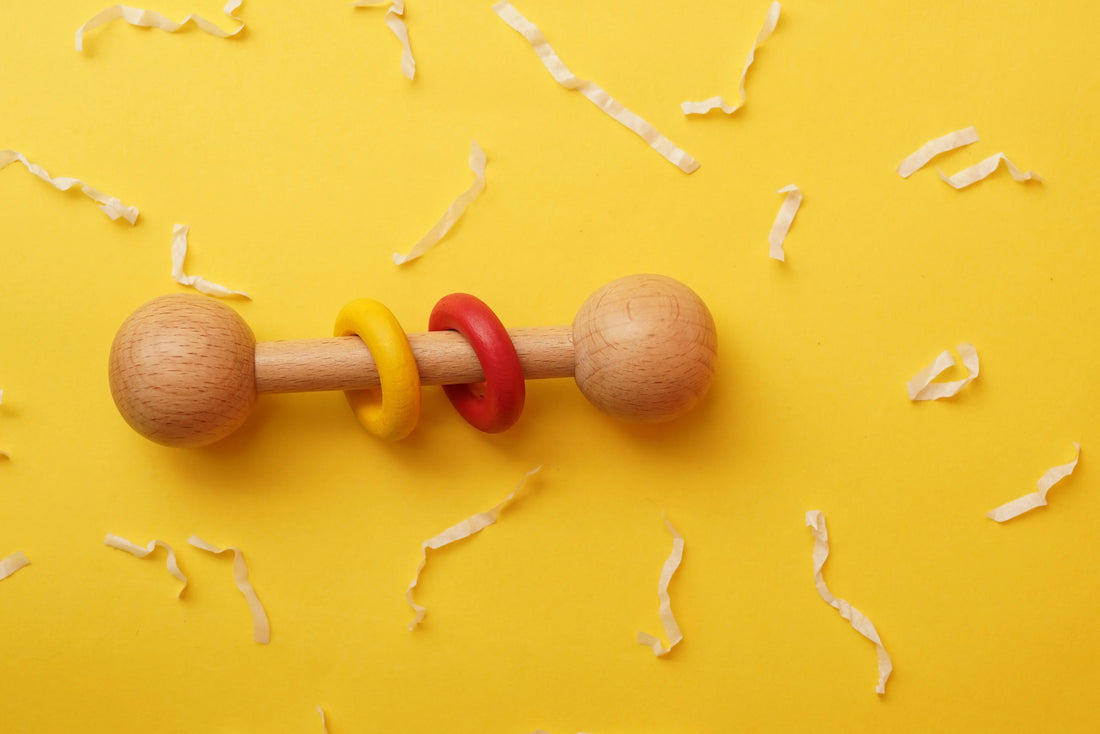 Wooden baby rattle with red and yellow rings on yellow background, Montessori toy