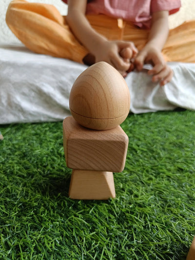 Child sitting on grass with natural wooden Montessori building blocks