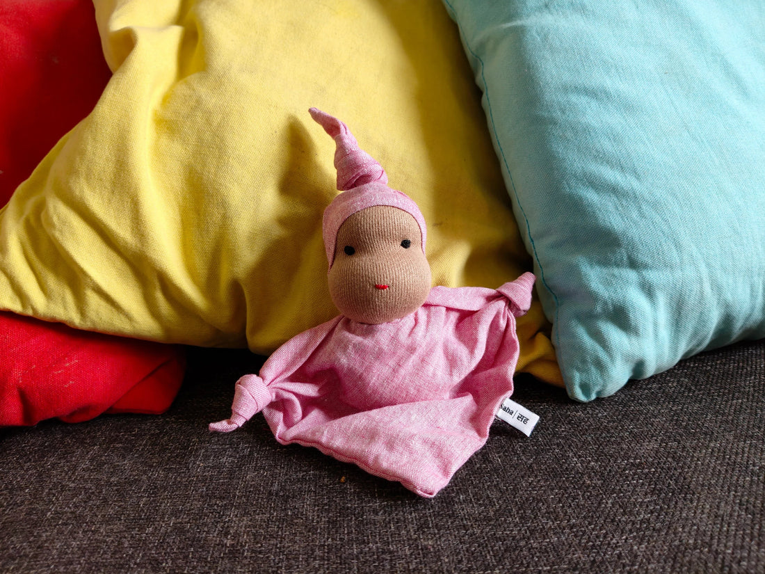 Waldorf style handmade cloth doll in pink outfit on sofa with colorful pillows