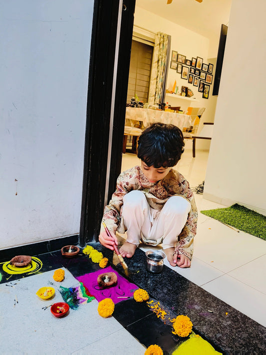 Child wearing traditional clothes creating colorful Diwali rangoli with marigold flowers and diyas
