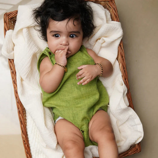 Newborn baby in a green organic cotton romper lying in a wicker basket