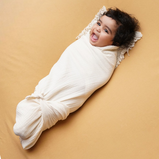 Newborn baby peacefully sleeping while wrapped in a soft, cotton swaddle blanket, lying on a bed with natural lighting