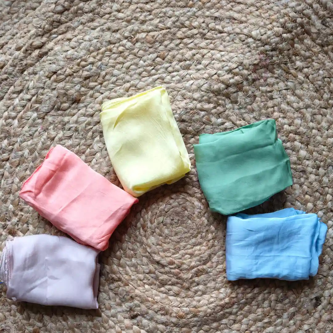 Soft cotton baby clothes in pastel pink, yellow, green, blue, and lavender on woven rug