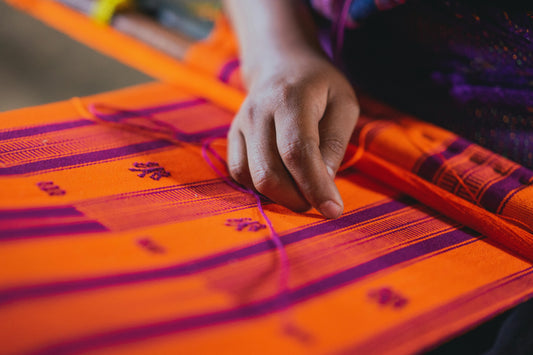 Hand weaving bright orange and purple khadi cotton fabric on a traditional loom