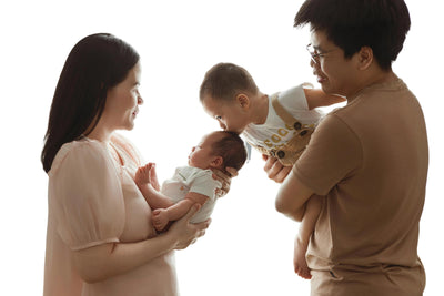 Smiling family with toddler and newborn in soft cotton baby outfits, white background