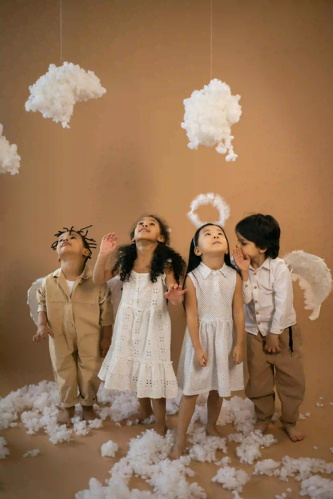 Kids in angel costumes with wings and halos, wearing khadi and cotton clothes, standing among clouds