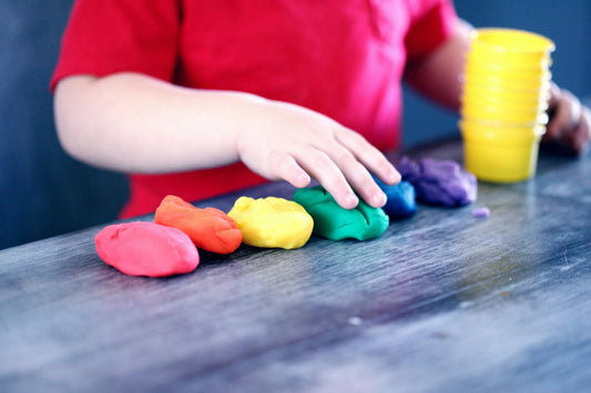 Child playing with colorful Montessori playdough, yellow cups on wooden table, early learning activity