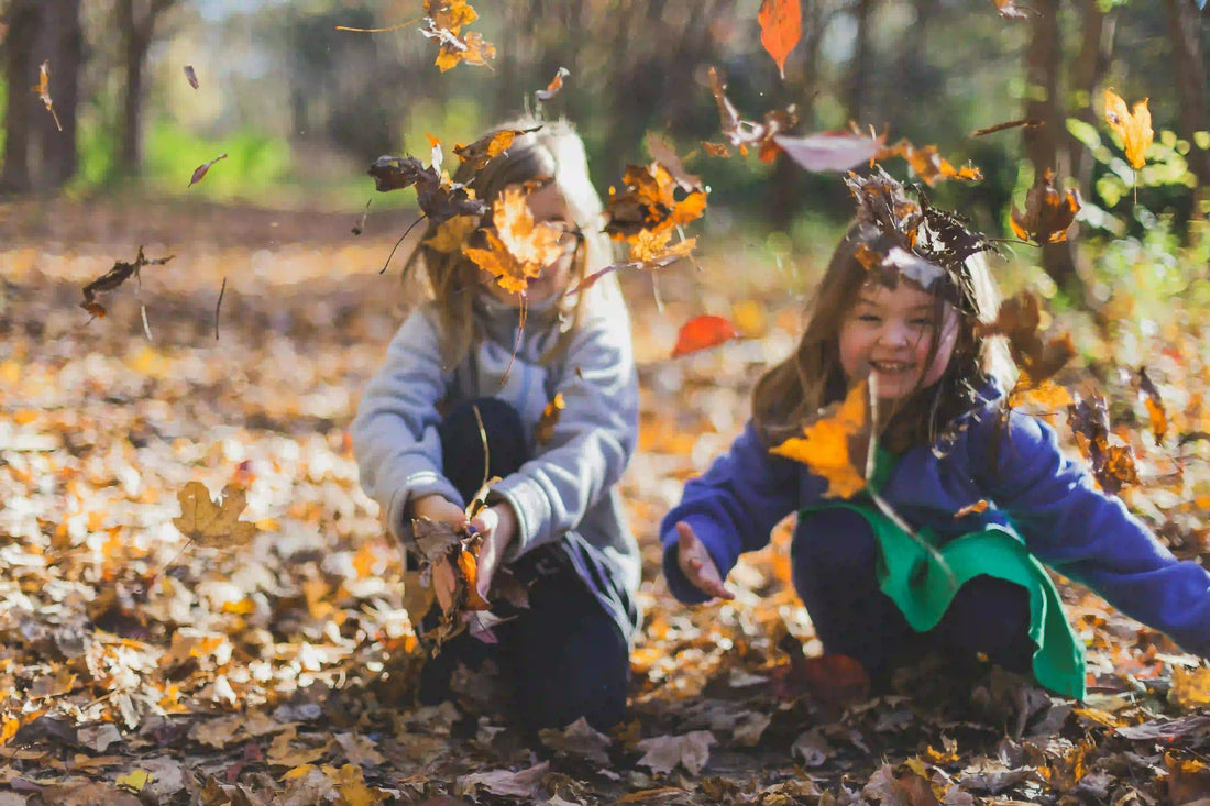 Two kids playing in autumn leaves outdoors, wearing colorful clothes, smiling and laughing