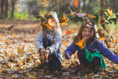 Two kids playing in autumn leaves outdoors, wearing colorful clothes, smiling and laughing