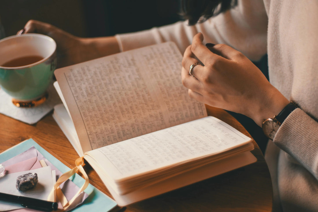Person journaling at a wooden table with tea, pen, and stationery, cozy indoor setting