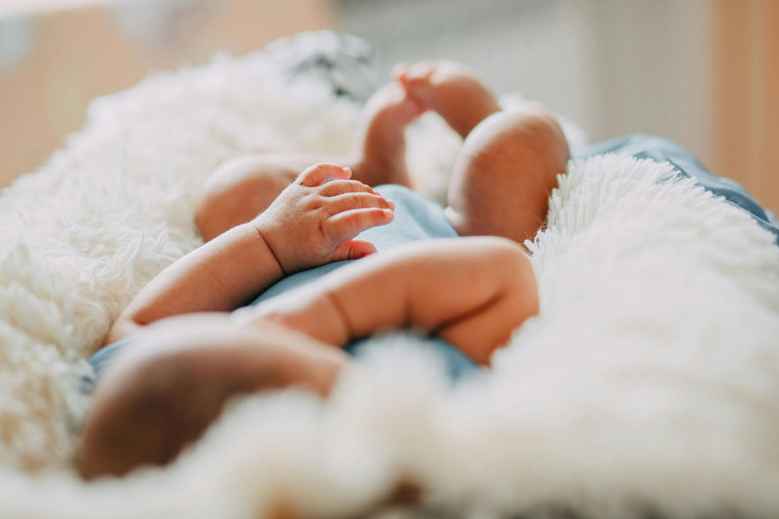 Newborn baby in organic cotton clothes resting on a soft white blanket, natural light