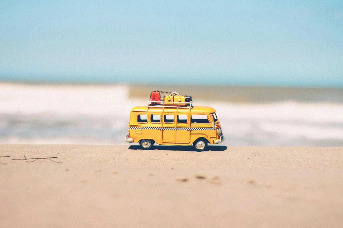 Yellow wooden toy van with luggage on roof, on sandy beach, educational toy