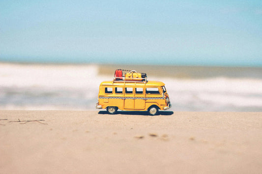 Yellow wooden toy van with luggage on roof, on sandy beach, educational toy