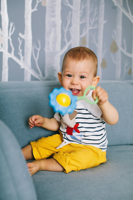 Smiling baby in yellow shorts holding a flower-shaped educational toy on a couch
