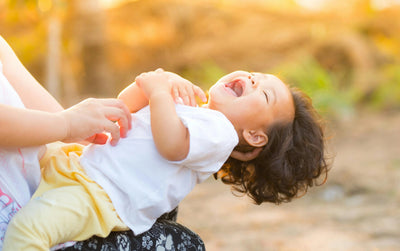 Smiling toddler wearing organic cotton clothes laughing outdoors in sunlight