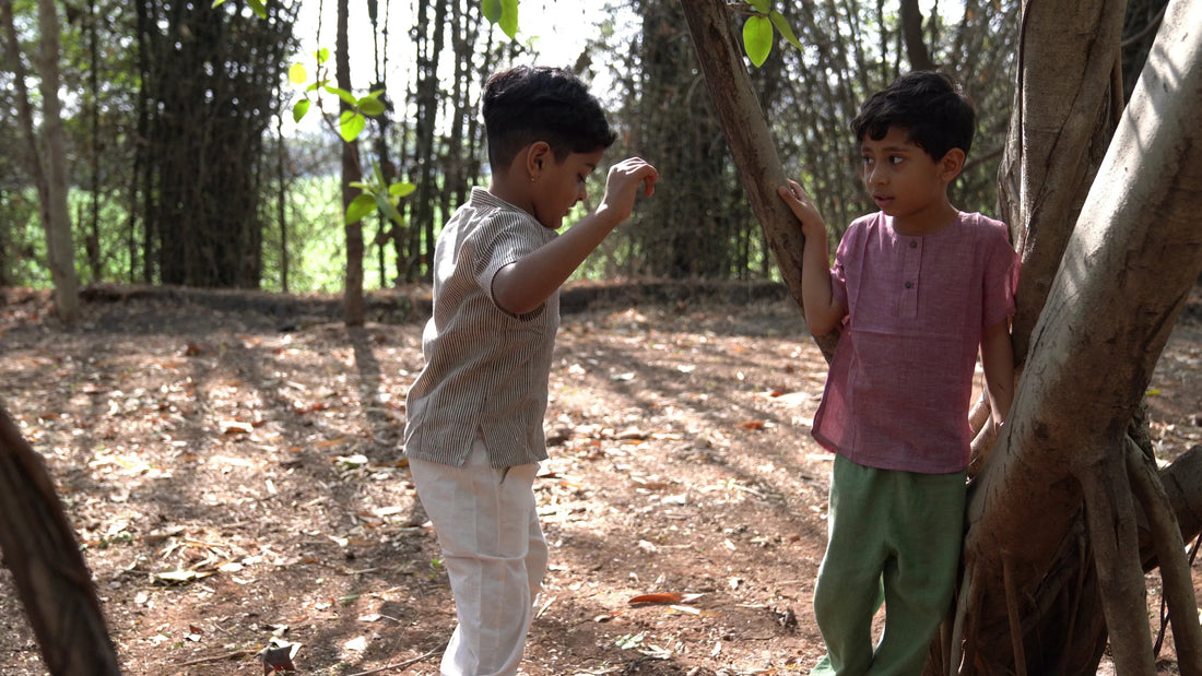 Two young children in cotton clothes playing outdoors among trees and natural sunlight