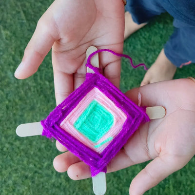Hand holding colorful yarn-wrapped popsicle stick craft, Waldorf-inspired open-ended toy for kids