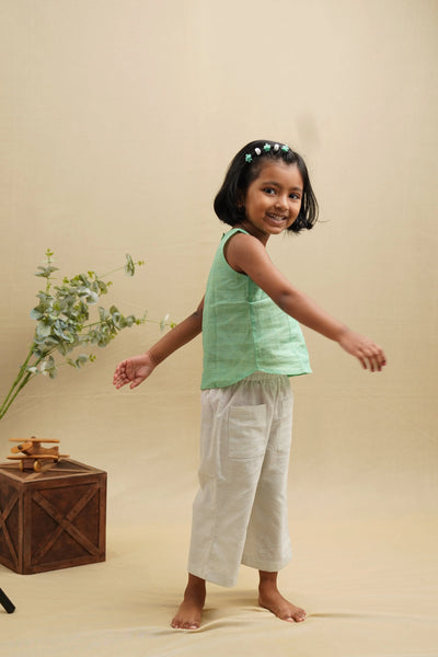Smiling girl in mint green khadi top and cream organic cotton pants, barefoot, indoor