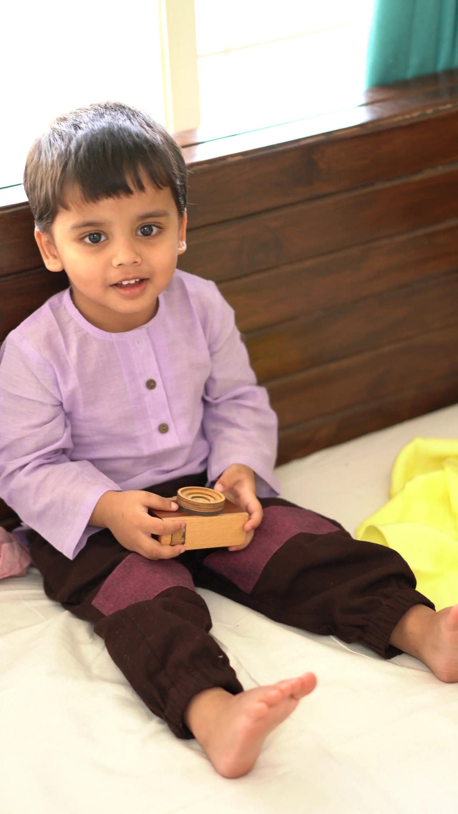 Child playing with wooden toy camera, wearing cotton clothes for free play and comfort