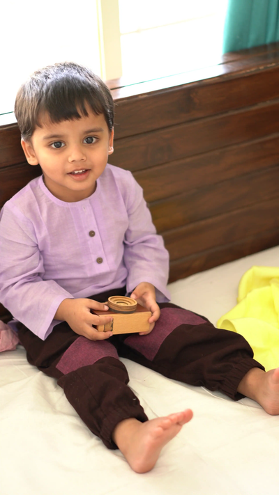 Child playing with wooden toy camera, wearing cotton clothes for free play and comfort
