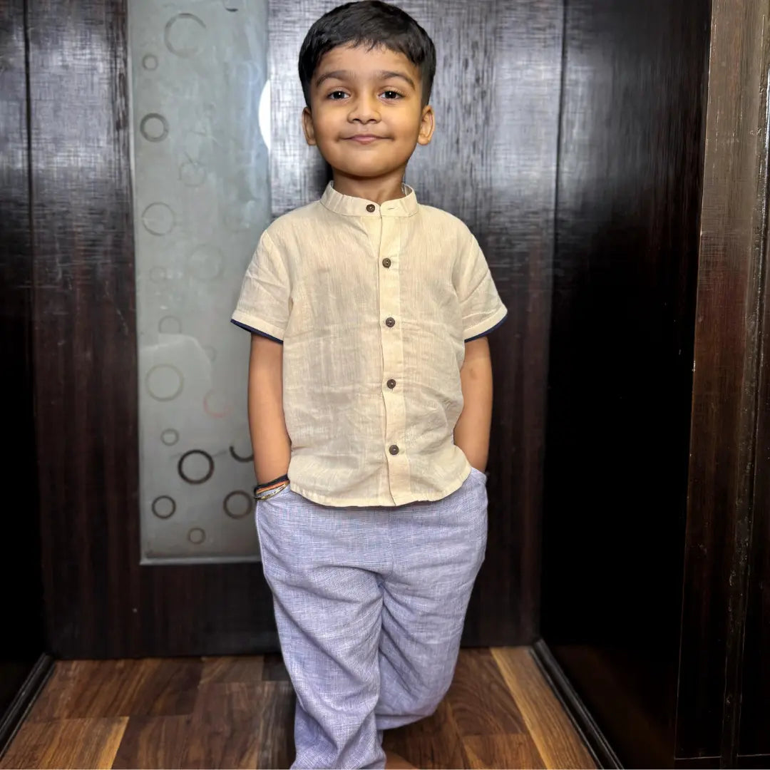 Child wearing a beige shirt and purple pants standing in front of a wooden door