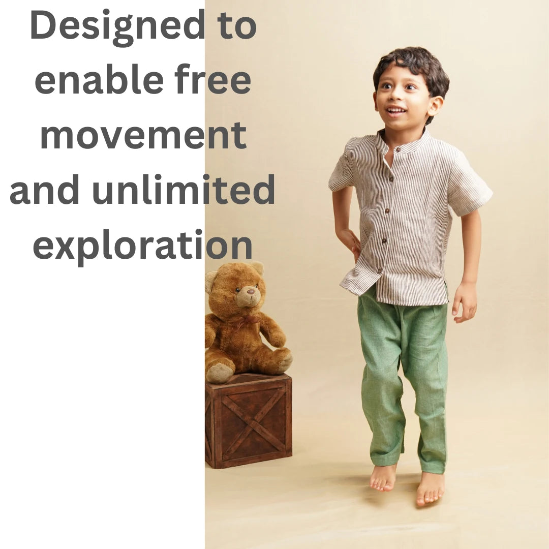 A young boy in a light beige linen short-sleeve kurta and green trousers, standing barefoot on a beige studio floor