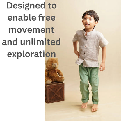 A young boy in a light beige linen short-sleeve kurta and green trousers, standing barefoot on a beige studio floor