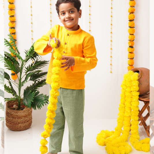 Child in a yellow khadi outfit holding a long yellow decorative garland against a white background with plants.