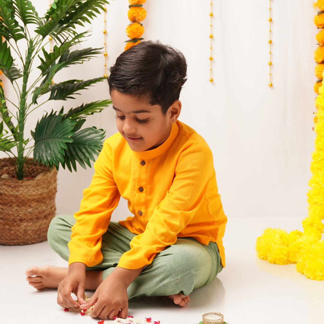 Child in a yellow khadi kurta sitting on the floor with decorative elements in the background