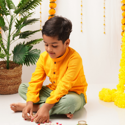 Child in a yellow khadi kurta sitting on the floor with decorative elements in the background