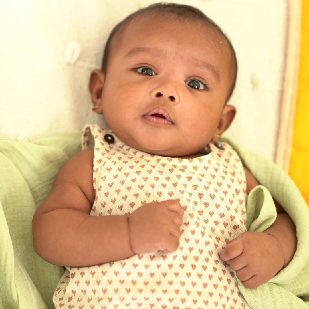 Baby wearing a heart print Cotton Onesie made from breathable handspun khadi fabric while lying comfortably on a soft blanket