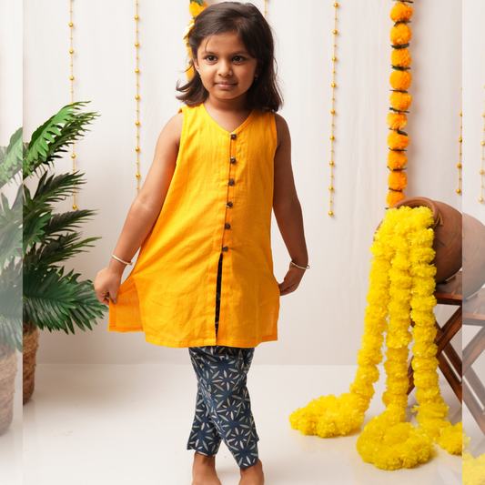 Young girl in a yellow khadi kurta with blue pants standing in a decorated room.