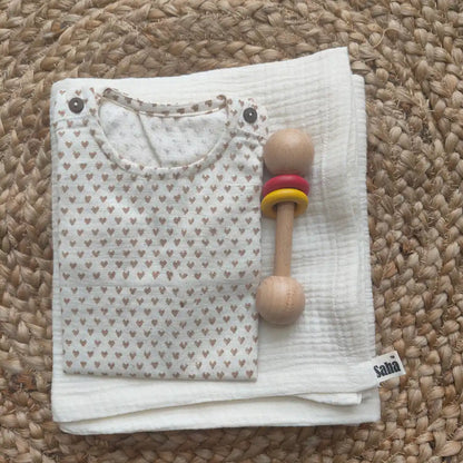 Folded baby outfit with a wooden rattle on a muslin swaddle