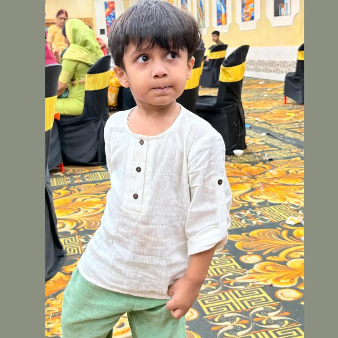 Child in a white shirt and green pants standing on a patterned floor 