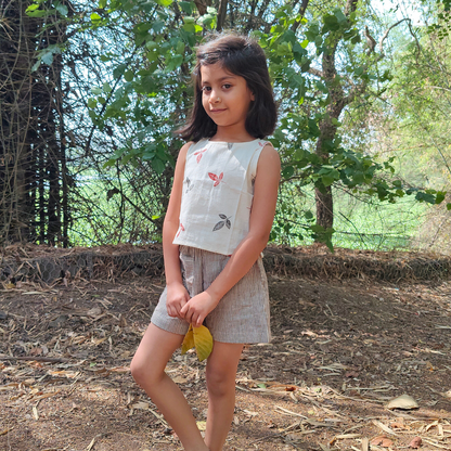 A girl wearing a beige floral crop top and stripe shorts set in pure cotton standing outdoors.