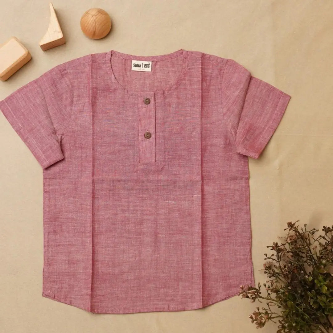 Pink short-sleeve kurta on a beige background with wooden blocks and plants.