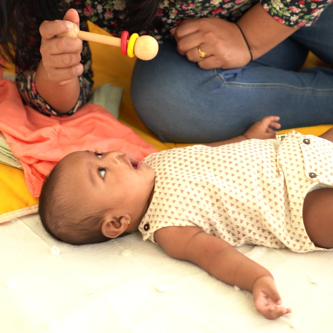 Baby relaxing in a heart print Cotton Onesie while engaging with a wooden toy during tummy time and sensory play