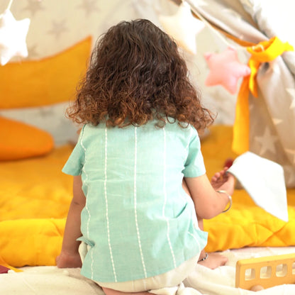 Back view of a child wearing a breathable mint green handloom cotton shirt with subtle white striped detailing while seated in a play space