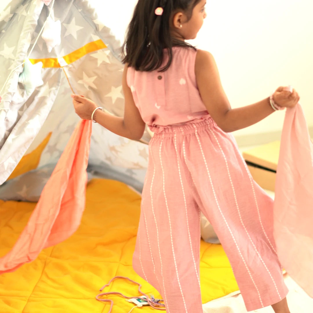 Back view of a girl wearing a breathable pink handloom cotton coord set with striped relaxed-fit pants near a play tent
