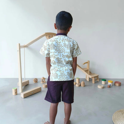 Back view of a child wearing a cream khadi short kurta with intricate Warli handblock printing paired with dark Ikat shorts.