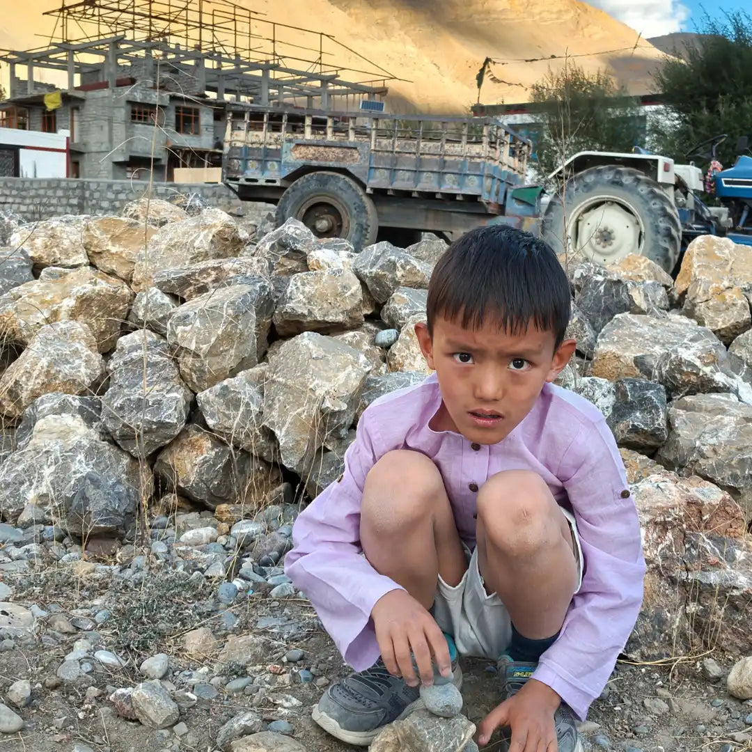 Child in a cotton shirt and shorts on rocks with construction vehicles and mountains in the background