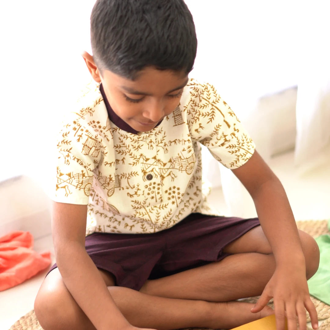 Boy sitting and playing comfortably in a handcrafted khadi short kurta set with traditional Warli block prints and soft cotton shorts.