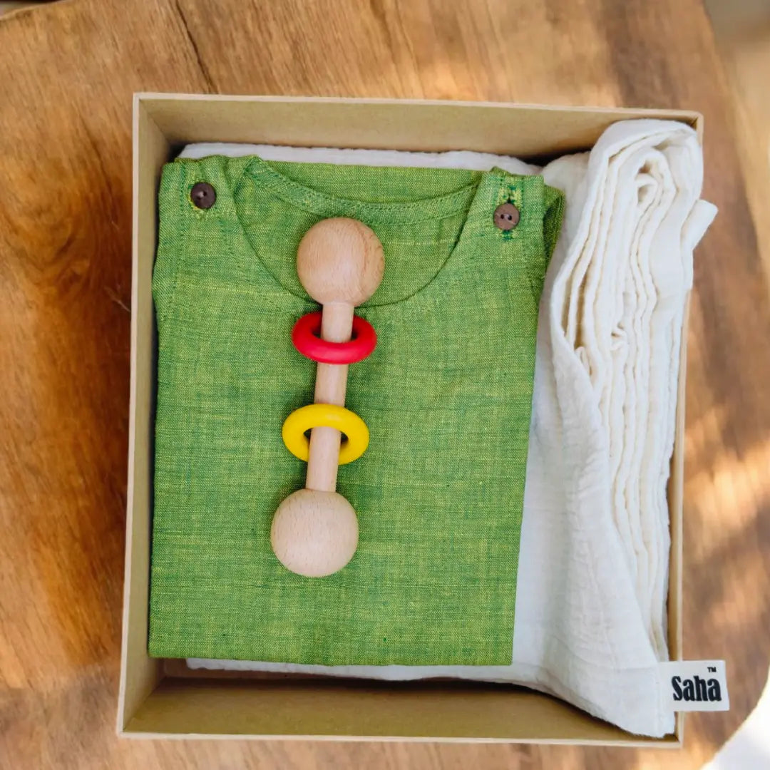 Colorful wooden baby rattle on a green baby outfit with white blanket in a box